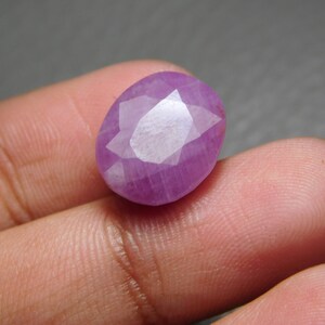 Puede incluir: Una gema rosa facetada, de forma ovalada. La gema tiene una superficie pulida con múltiples facetas que reflejan la luz. El color es un rosa vibrante, y la piedra parece estar sujeta por los dedos de una persona.