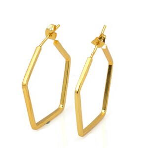 May include: A pair of gold hexagonal hoop earrings. The earrings are made of a smooth, shiny metal and have a simple, geometric design.