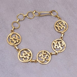 Puede incluir: Pulsera de oro con cinco dijes circulares con el símbolo Om. La pulsera tiene un cierre de broche.