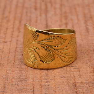 Op de afbeelding: Een ring van goudkleurig metaal met een brede band met een ingewikkeld bloemmotief. De ring is glad en gepolijst.