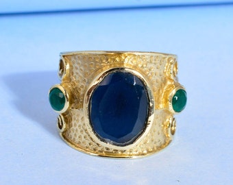 May include: A gold ring with a textured band and a large blue oval gemstone. Two smaller green gemstones are set on either side of the main stone.