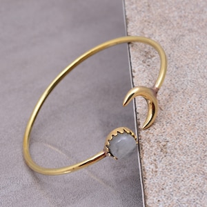 May include: A gold bangle bracelet with a crescent moon charm and a gray stone accent.