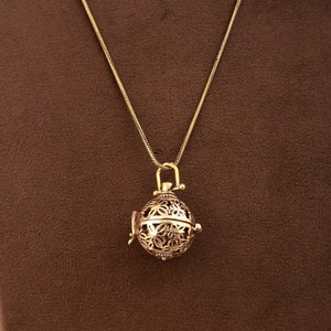 May include: A gold chain necklace with a delicate, ornate pendant. The pendant is a round, openwork cage with a floral design.