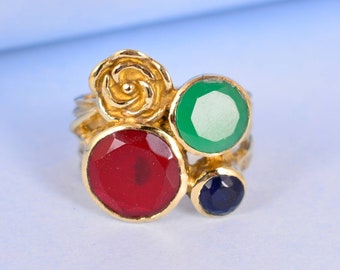 May include: A gold ring with a red, green, and blue gemstone setting. The ring features a rose design.