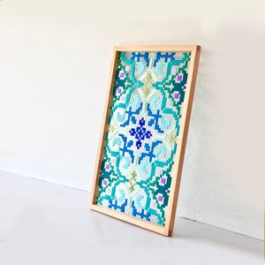 May include: A framed wall hanging with a colorful geometric pattern in shades of blue, green, and purple. The pattern is made up of small squares and rectangles, creating a complex and intricate design.