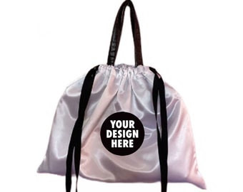 Könnte beinhalten: Ein satinfarbener Kordelzugbeutel in Hellrosa mit schwarzen Trägern und Kordeln. Ein schwarzer Kreis mit dem Text "YOUR DESIGN HERE" befindet sich in der Mitte der Tasche. Ein kleiner herzförmiger Anhänger hängt über der Tasche.