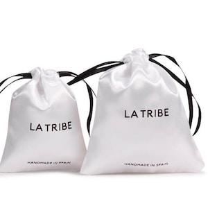 May include: Two white satin drawstring bags with black drawstrings. The larger bag has "LA TRIBE" and "HANDMADE IN SPAIN" printed on the front. The smaller bag has "LA TRIBE" and "HANDMADE IN SPAIN" printed on the front.