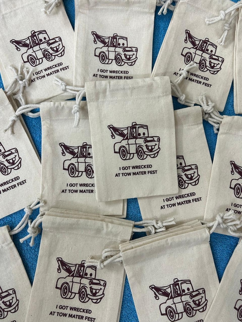 Puede incluir: Una colecci&oacute;n de peque&ntilde;as bolsas de tela blanca con cierres de cord&oacute;n marr&oacute;n. Cada bolsa presenta una imagen de dibujos animados de una gr&uacute;a roja con el texto "I got wrecked at Tow Mater Fest".