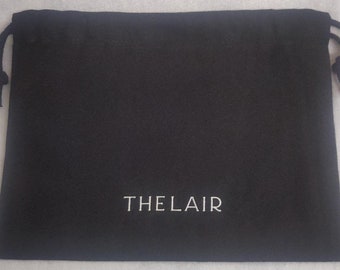 Könnte beinhalten: Eine schwarze Kordeltasche mit dem Aufdruck "THE LAIR" in weiß auf der Vorderseite.