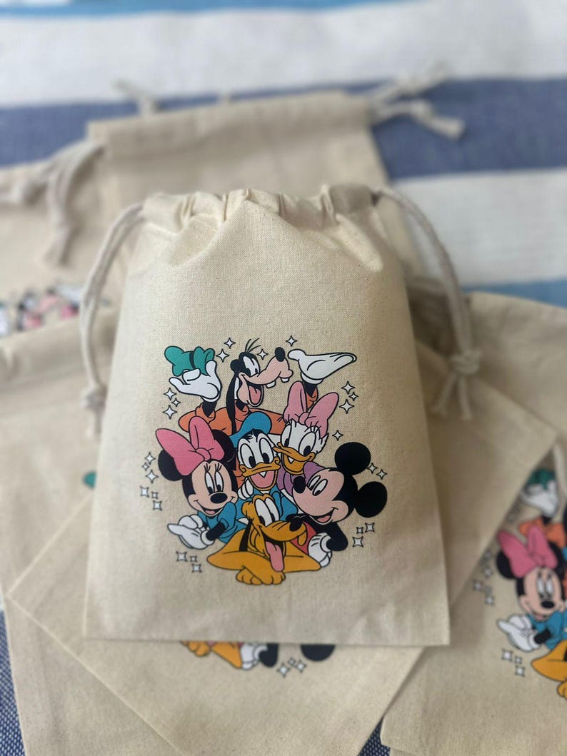 Op de afbeelding: Beige trekkoordzakken met een kleurrijke afbeelding van Disney-personages, waaronder Mickey Mouse, Minnie Mouse, Donald Duck en Goofy. De zakken zijn gemaakt van een natuurlijke stof en zijn ideaal voor feestartikelen of kleine cadeaus.