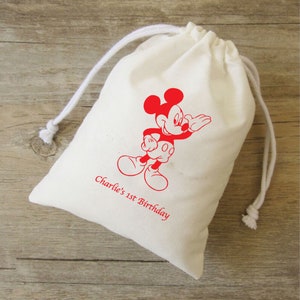Może przedstawiać: Biała bawełniana torba ze sznurkiem, ozdobiona czerwoną postacią Myszki Miki i tekstem "Charlie's 1st Birthday".