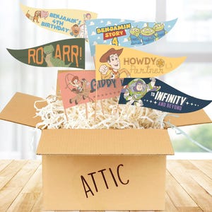 May include: A cardboard box labelled "ATTIC" filled with paper shreds, holding several decorative pennant flags. The flags feature cartoon characters and phrases like "ROARR!", "Howdy Partner", and "To Infinity and Beyond".