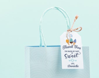 May include: A light blue gift bag with a white and blue patterned design. The bag has a white tag attached with the text "Thank You for making my party so Sweet Love, Danielle".