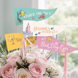 May include: A floral arrangement in a blue vase with pink and white roses, accented by decorative pennant flags. The flags feature phrases like "Under the Sea" and "Best Day Ever," with related illustrations. A pink candle is also visible.