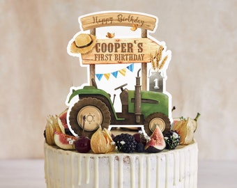 May include: A white cake with white frosting and a green tractor cake topper. The topper has a sign that says "Happy Birthday Cooper's First Birthday".