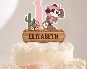 May include: A pink and brown cake topper with a cartoon cowgirl character, a cactus, a wagon wheel, and a wooden sign that says "ELIZABETH".