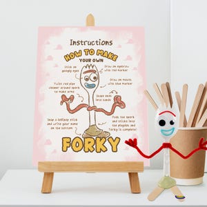 May include: A pink instructional sign on a wooden easel titled How to Make Your Own Forky, featuring a diagram with text steps and a physical Forky character made of a white spork, red pipe cleaner arms, googly eyes, and a clay base.