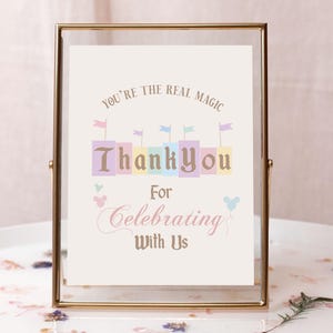 May include: A gold-framed sign with the text "You're the real magic" and "Thank you for celebrating with us". The sign features a colorful castle illustration and Mickey Mouse ears.