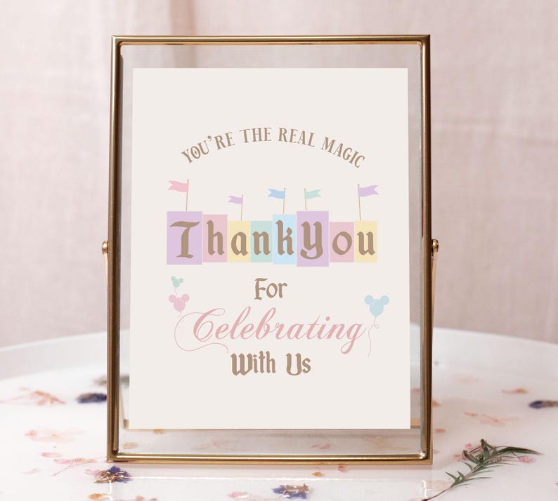May include: A gold-framed sign with the text "You're the real magic" and "Thank you for celebrating with us". The sign features a colorful castle illustration and Mickey Mouse ears.