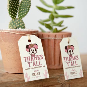 Pode incluir: Duas etiquetas de presente brancas com um personagem de desenho animado rosa e marrom usando um chapéu de cowboy. O texto nas etiquetas diz "Thanks Y'all" e "For celebrating with me! Love, Kelly".