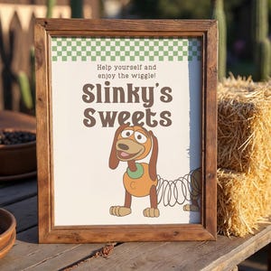 May include: A framed sign with the text "Slinky's Sweets" and a cartoon dog illustration. The sign has a green and white checkered border and the words "Help yourself and enjoy the wiggle!" The frame is made of wood.