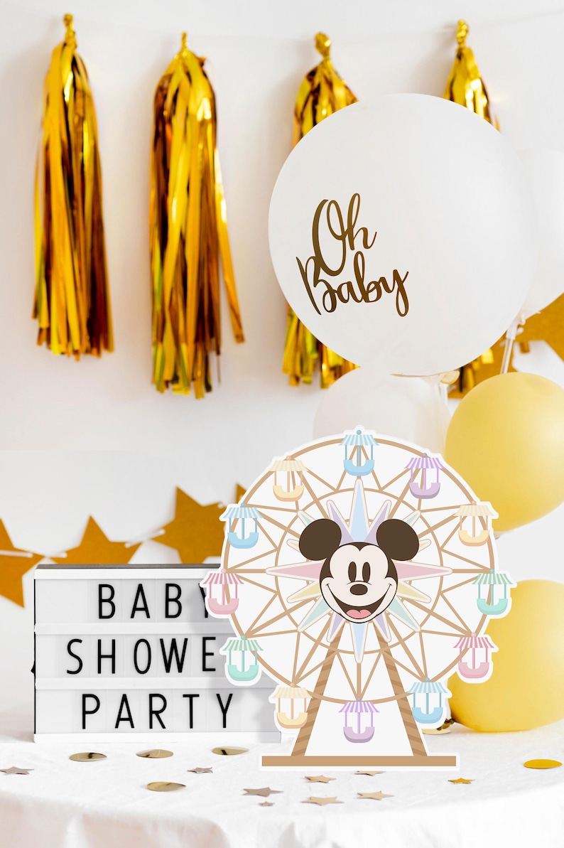 May include: A white balloon with gold lettering that says "Oh Baby" and a Mickey Mouse Ferris wheel centrepiece with pastel coloured gondolas. The background includes gold tassel streamers and a white letter board that says "Baby Shower Party".