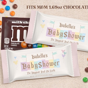 Könnte beinhalten: Eine personalisierte weiße und rosafarbene Süßigkeitenverpackung mit dem Text "Isabella's Baby Shower" und "The Happiest Treat On Earth". Die Verpackung ist für einen 1,69 oz M&M Schokoladenriegel konzipiert.