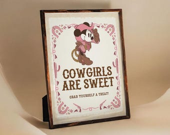 Puede incluir: Una impresión enmarcada con una imagen de dibujos animados de Mickey Mouse vestido de vaquera. La impresión tiene un esquema de color rosa y marrón y dice "Cowgirls are sweet. Grab yourself a treat!"