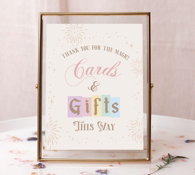May include: A gold-framed sign with a white background and pink and gold text that reads "Thank you for the magic! Cards & Gifts This Way". The sign is decorated with fireworks and stars.