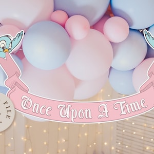 May include: A pink and blue banner with the text "Once Upon A Time" in white. The banner is decorated with two blue birds on each end. The banner is hanging from a ceiling with pink and blue balloons in the background.