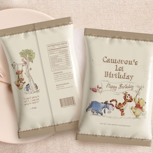 May include: Two beige party favor bags with a Winnie the Pooh theme. One bag features Pooh and friends on a swing, the other says "Cameron's 1st Birthday" with "Happy Birthday" and illustrations of Pooh, Tigger, and Eeyore.