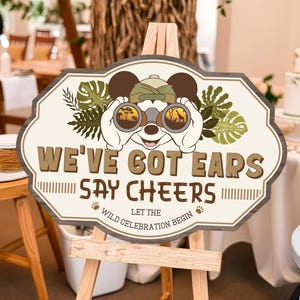 Könnte beinhalten: Ein Holzschild mit Safari-Thema, das eine Cartoon-Mausfigur mit Safarihut und Fernglas zeigt. Auf dem Schild steht "WE'VE GOT EARS SAY CHEERS" mit dem Text "LET THE WILD CELEBRATION BEGIN".