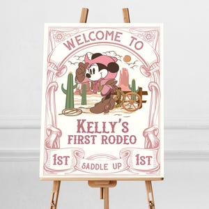 May include: A pink and white sign with a cartoon mouse wearing a cowboy hat and riding a horse. The sign says "Welcome to Kelly's First Rodeo 1st Saddle Up 1st".