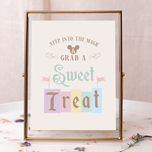 May include: A gold-framed sign with the text "Step into the magic & grab a sweet treat". The sign features a Mickey Mouse head icon and a colorful stack of blocks with the word "treat" in a decorative font.