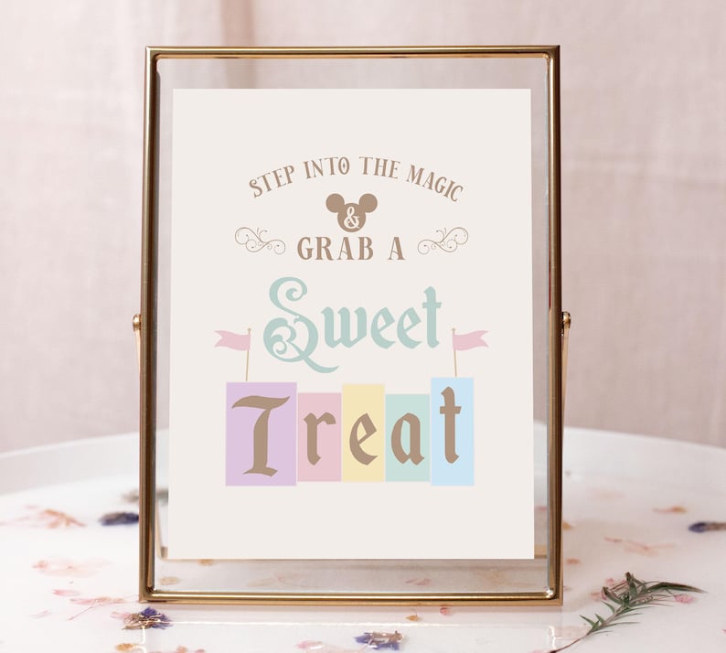 May include: A gold-framed sign with the text "Step into the magic & grab a sweet treat". The sign features a Mickey Mouse head icon and a colorful stack of blocks with the word "treat" in a decorative font.