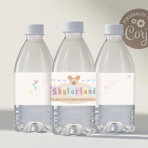 May include: Three clear plastic water bottles with personalized labels. The labels are white with a light blue, pink, and yellow color scheme. The labels feature a cartoon image of Mickey Mouse's head and the text "Skylarland Welcome to the Happiest Place on Earth".