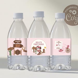 May include: Three clear plastic water bottles with pink labels. The labels feature a Wild West theme with signs, a cartoon character, and a wanted poster. The text on the labels includes "Welcome to Wild West" and "Kelly's First Rodeo".