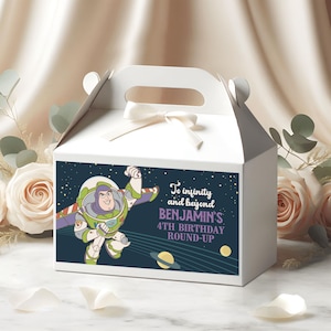 May include: White gable box with a handle and a bow. The box features a graphic of Buzz Lightyear from Toy Story, with the text "To infinity and beyond" and "Benjamin's 4th Birthday Round-Up."