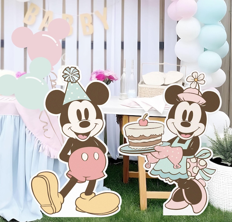 May include: Two cartoon character cutouts of Mickey Mouse and Minnie Mouse. Mickey Mouse is wearing a red and white hat and a red and white shirt. Minnie Mouse is wearing a pink and white dress and a pink and white hat. Minnie Mouse is holding a plate with a cake on it. The cake is decorated with a cherry on top.