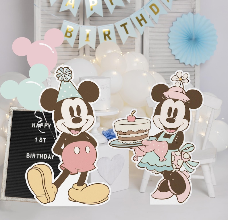 May include: Two cardboard cutouts of Mickey Mouse and Minnie Mouse dressed in party attire. Mickey is wearing a blue and white hat and a red shirt with black polka dots. Minnie is wearing a blue and white dress with white polka dots and a pink and white hat. Minnie is holding a plate with a layered cake with a red cherry on top. The text "Happy 1st Birthday" is visible on a black chalkboard.