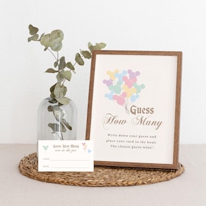 May include: A printable game card with a light brown frame and a light pink background. The card features a cartoon image of pastel colored balloons in the shape of Mickey Mouse heads. The text on the card reads "Guess How Many" in a decorative font. The card also includes instructions for the game, which is to guess how many balloons are in a jar.
