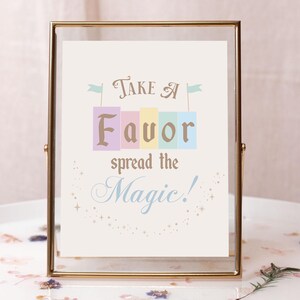 May include: A gold-framed sign with the text "Take a Favor spread the Magic!" in a whimsical font. The word "Favor" is spelled out in colorful blocks with flags on top.