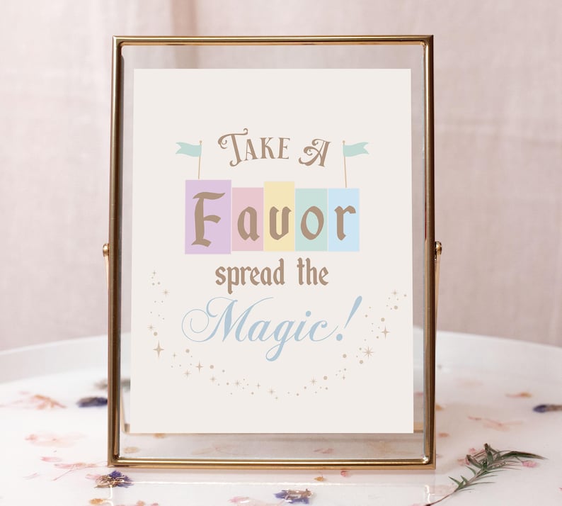 May include: A gold-framed sign with the text "Take a Favor spread the Magic!" in a whimsical font. The word "Favor" is spelled out in colorful blocks with flags on top.