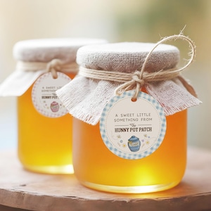 May include: Two glass jars filled with golden honey. Each jar has a burlap lid, twine, and a round tag that reads "A Sweet Little Something From The Hunny Pot Patch." The tags have a blue and white gingham border and a cartoon honey pot.