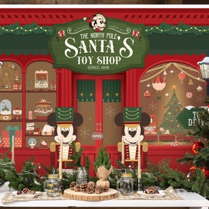 Puede incluir: Un telón de fondo navideño rojo y verde con una fachada de tienda de juguetes que presenta a Mickey Mouse como un soldado de juguete. La tienda se llama "The North Pole's Santa's Toy Shop" y tiene un letrero que dice "Since 1928". Hay dos soldados de juguete de Mickey Mouse en una mesa frente al telón de fondo, junto con un árbol de Navidad y otras decoraciones.