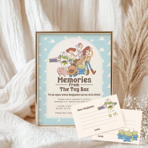 May include: A framed print with a light blue background and cartoon characters from "Toy Story." The text reads "Memories from The Toy Box" and "To be open when Benjamin turns 18 in 2043!" Includes two small cards with "Dear Benjamin" and "Love" printed on them.