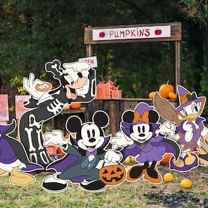 Pode incluir: Um grupo de personagens da Disney vestidos com fantasias de Halloween estão em frente a uma barraca de abóboras. Mickey Mouse está vestido de vampiro, Minnie Mouse de bruxa, Donald Duck de diabo, Pateta de esqueleto, Daisy Duck de bruxa e Pluto de fantasma.