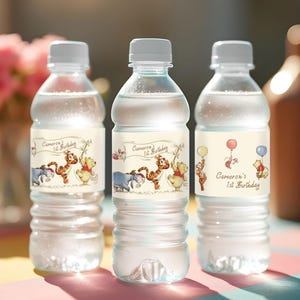 May include: Three clear plastic water bottles with white caps. Each bottle has a label featuring Winnie the Pooh characters and the text "Cameron's 1st Birthday". One label shows balloons.