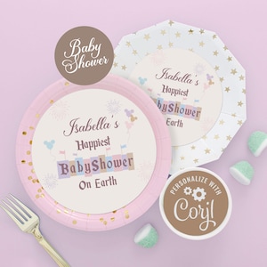 以下が含まれることがあります： 「Isabella's Happiest Baby Shower On Earth」と書かれたピンクとゴールドのベビーシャワープレート。金のフォークとキャンディーも表示されています。「Personalize with Coril」と書かれた丸いステッカー。