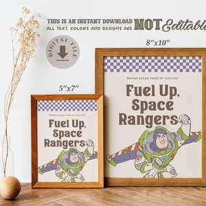 May include: Two framed prints with a wooden finish. The prints feature the text "Fuel Up, Space Rangers" and an illustration of Buzz Lightyear. The larger print is 8"x10", and the smaller is 5"x7".